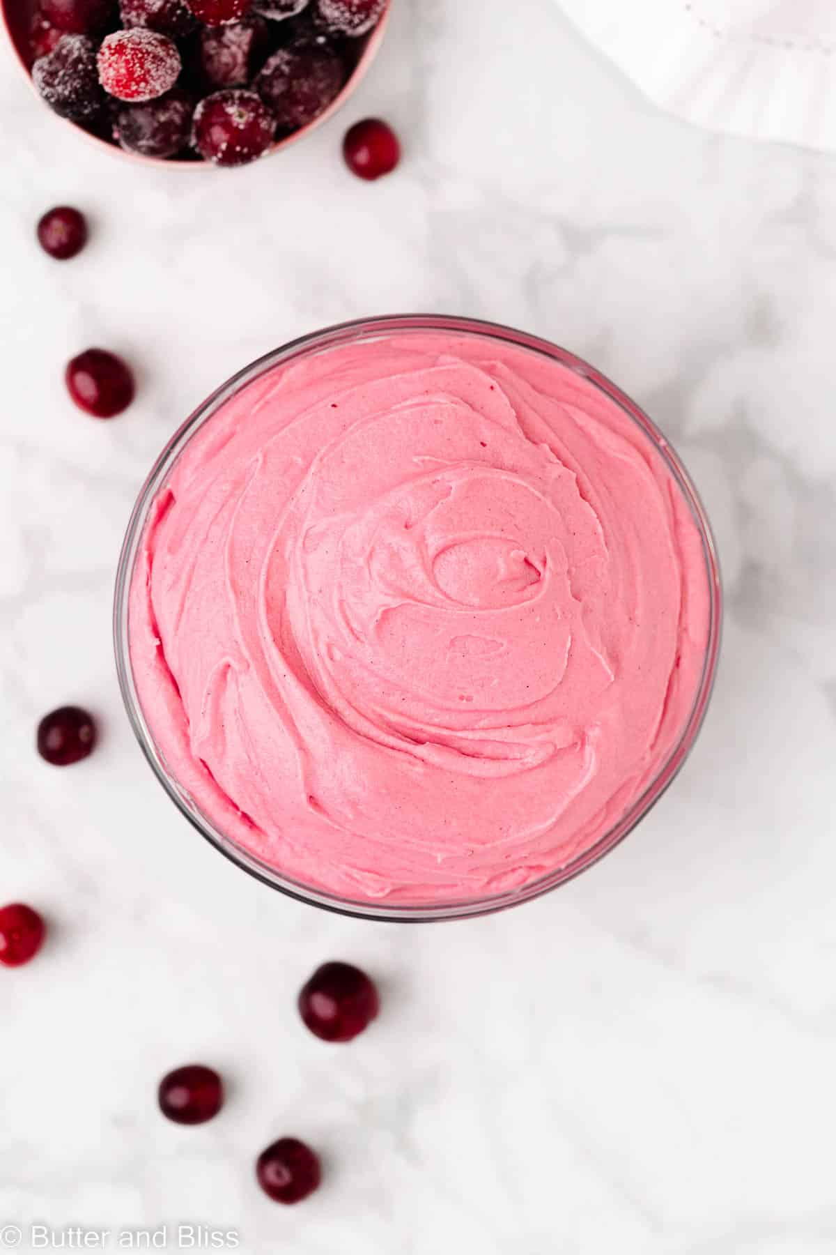 Glass bowl filled with creamy cranberry frosting with fresh cranberries arranged around it.