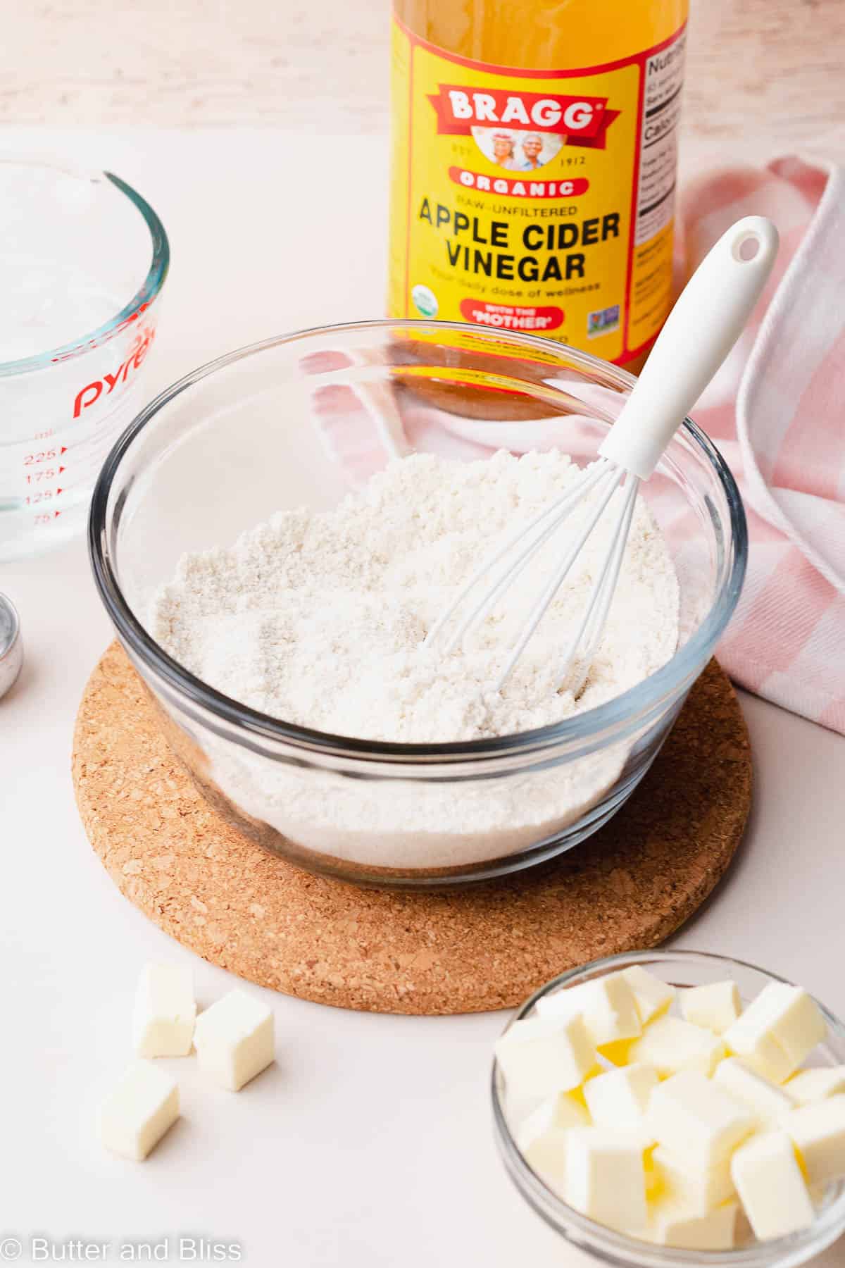 Gluten free flour in a bowl with a whisk and wet ingredients to be added.