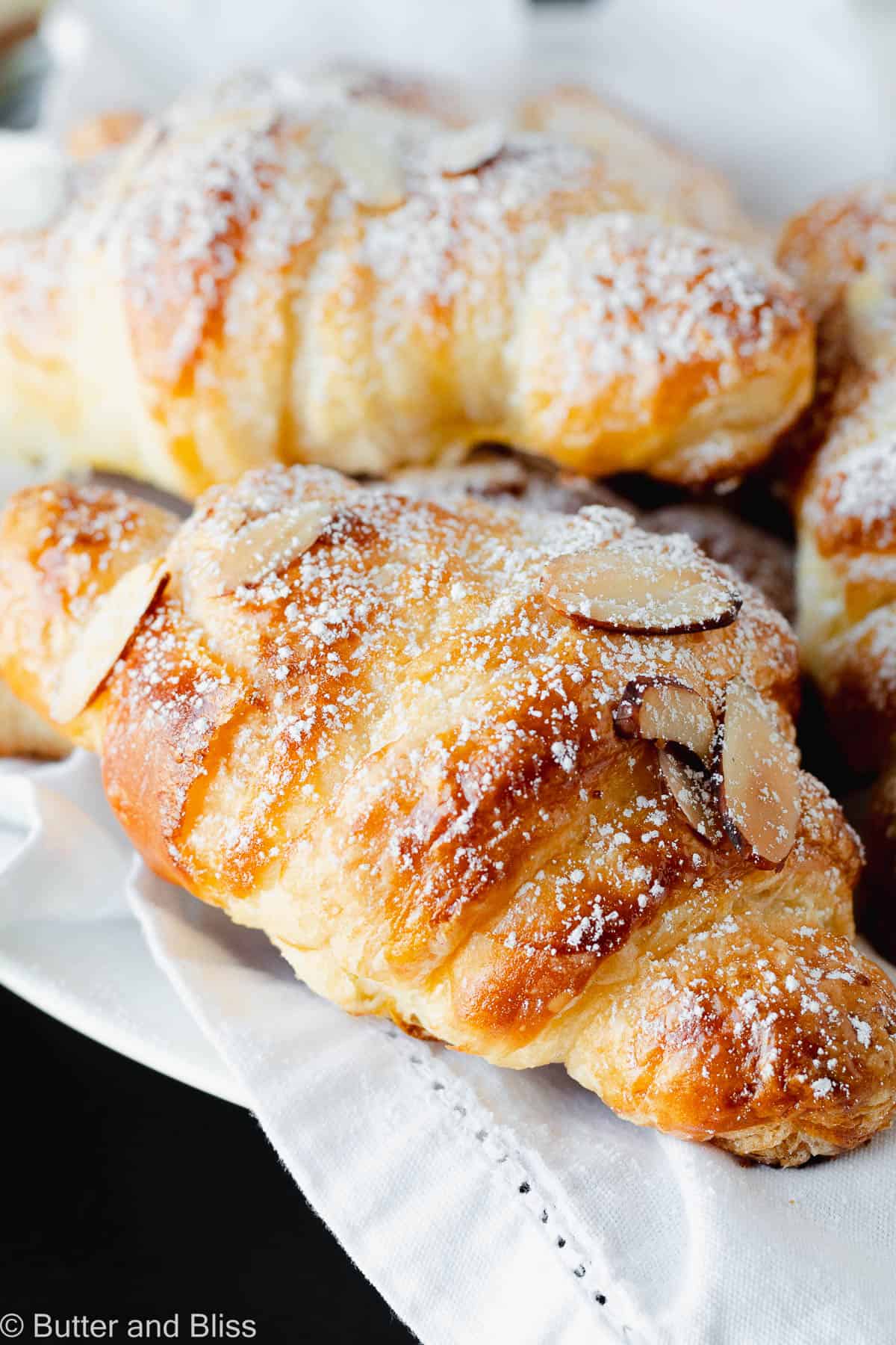 Flaky almond croissant on a white napkin with powdered sugar sprinkle.