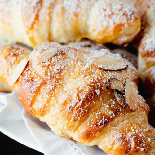 Flaky almond croissant on a white napkin with powdered sugar sprinkle.
