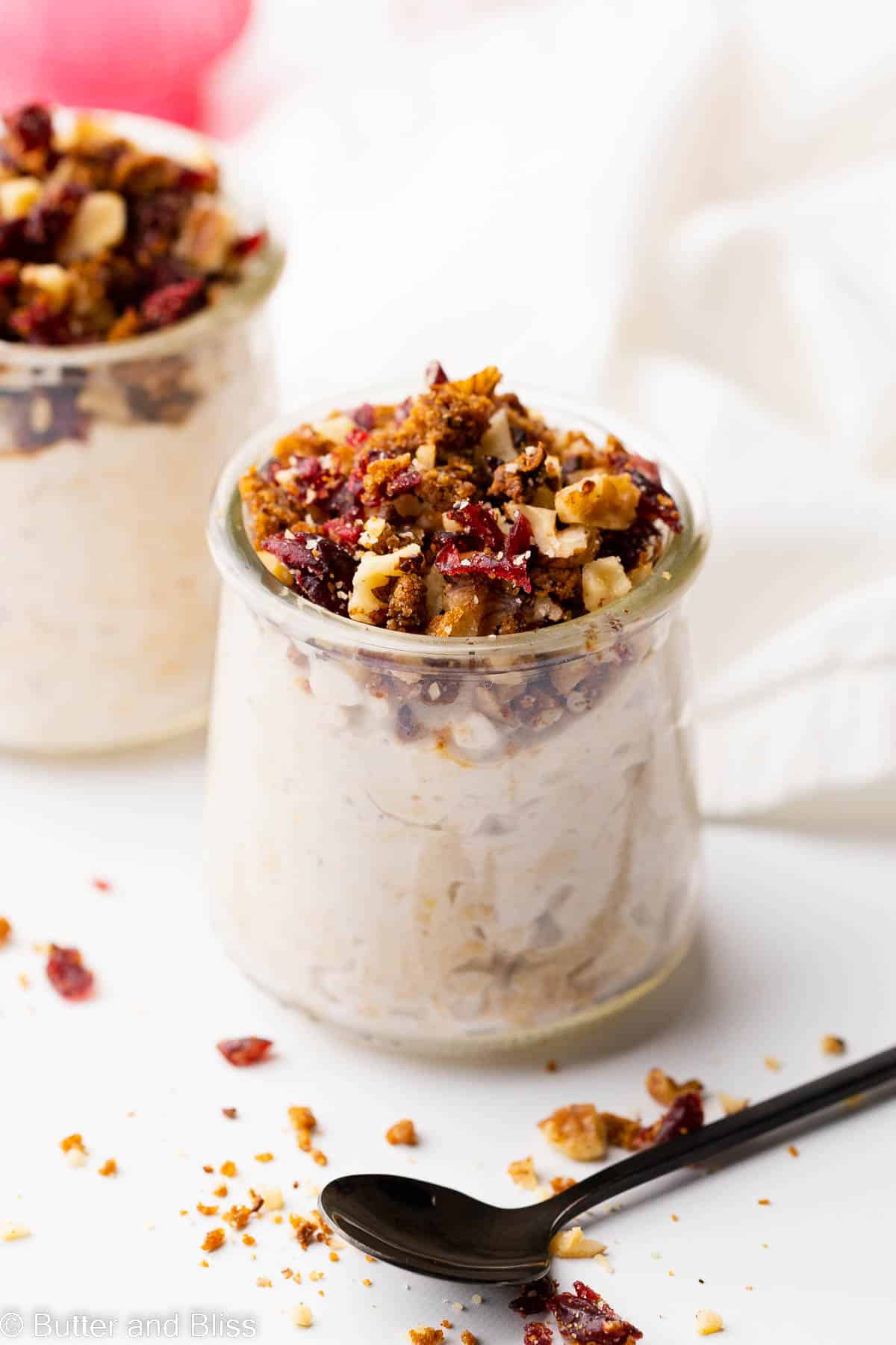 Two serving glasses filled with creamy eggnog overnight oats topped with a cranberry crumble.