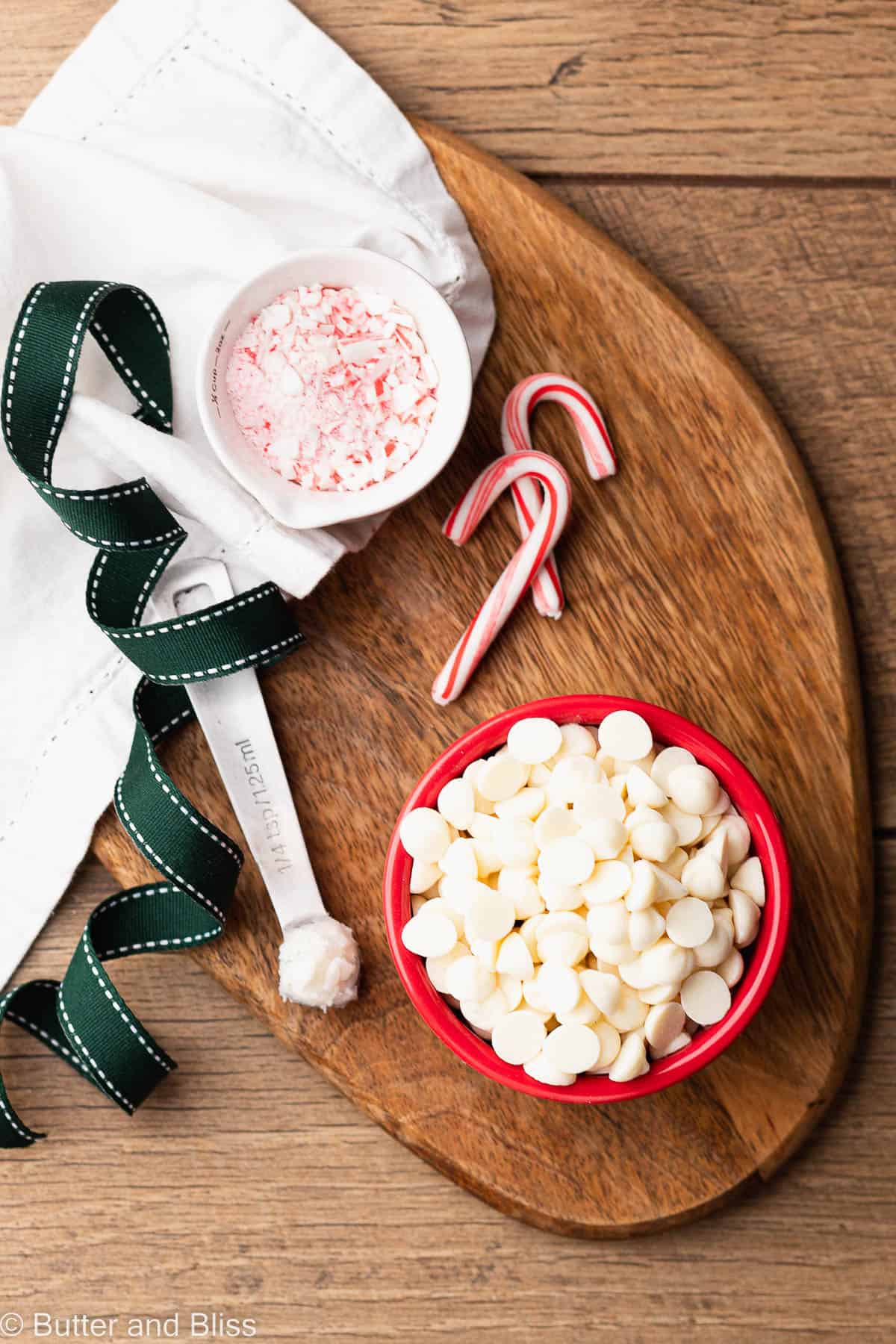 White chocolate chips and peppermint candies in small decorative bowls arranged on a wood table.
