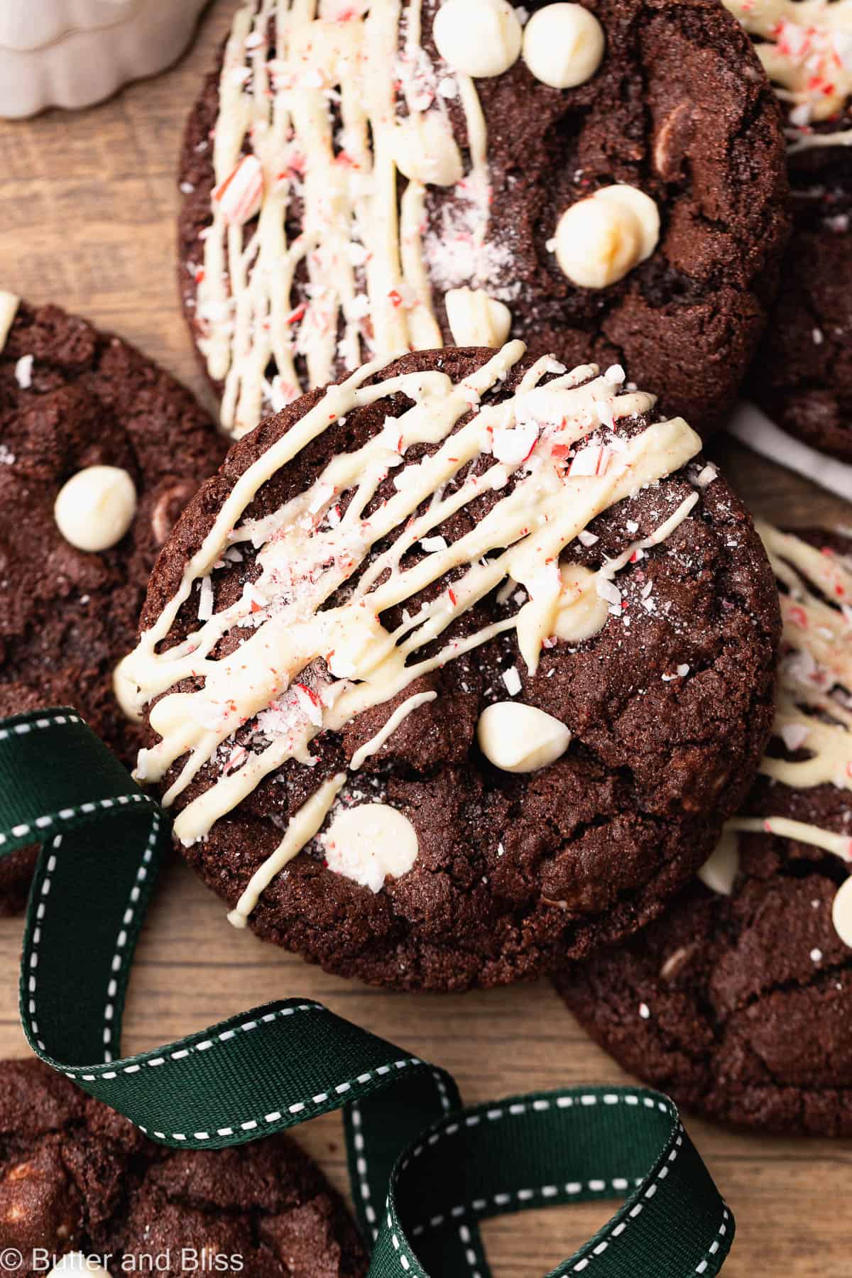Gluten free chocolate peppermint cookies with white chocolate drizzle arranged on a wood table.