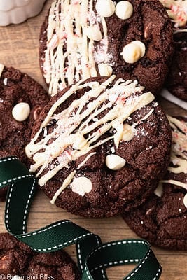 Gluten free chocolate peppermint cookies with white chocolate drizzle arranged on a wood table.
