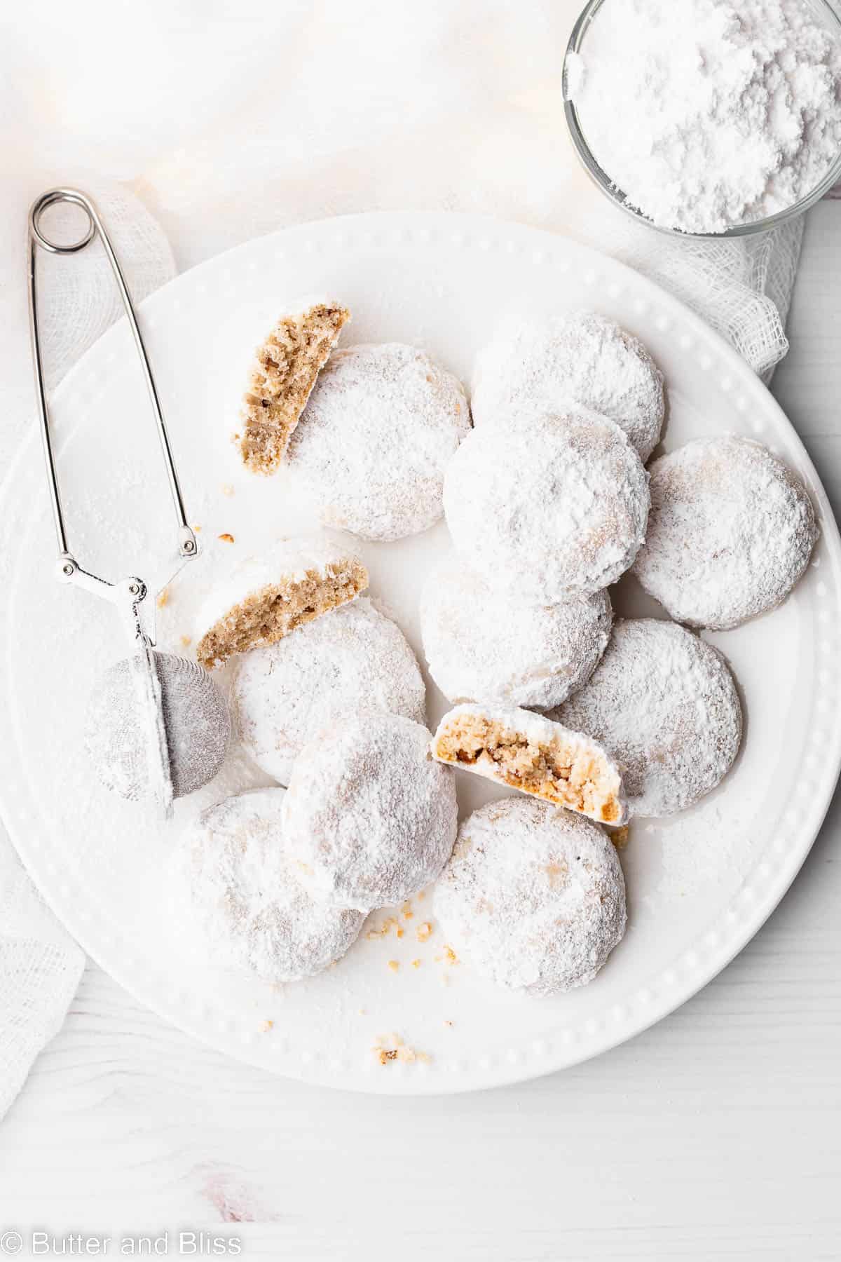 A white plate of snow white snowball cookies with powdered sugar.