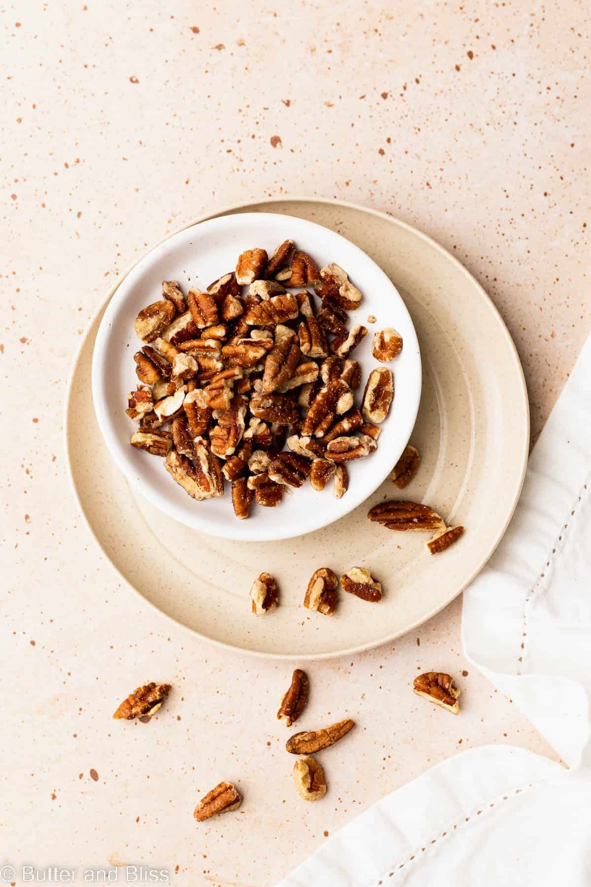 Chopped pecans in a small white dish set on a table.