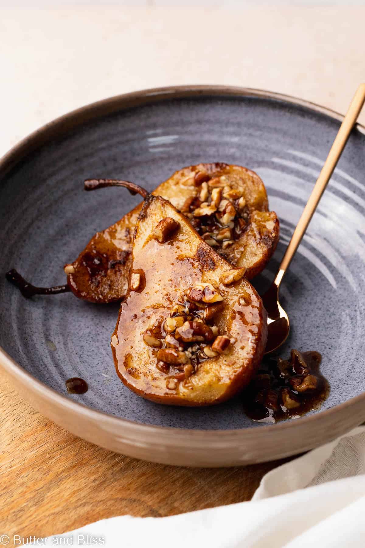 A serving of freshly baked pears covered in maple caramel in a blue bowl on a table.