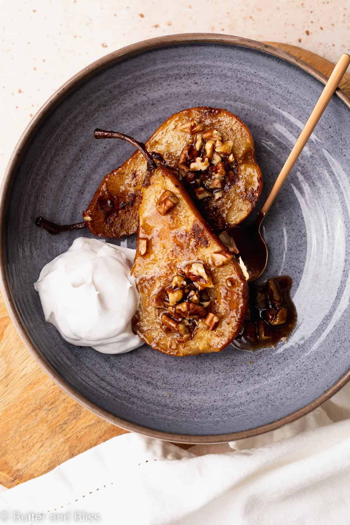 Baked pears in a serving bowl with a dollop of whipped cream set on a table.