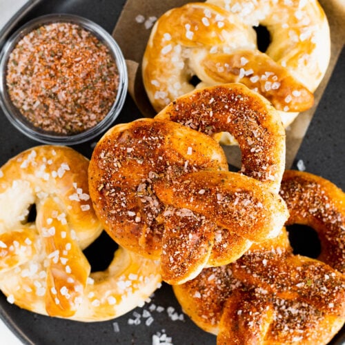 Soft baked pretzels sprinkled with zesty seasoning on a dark plate.