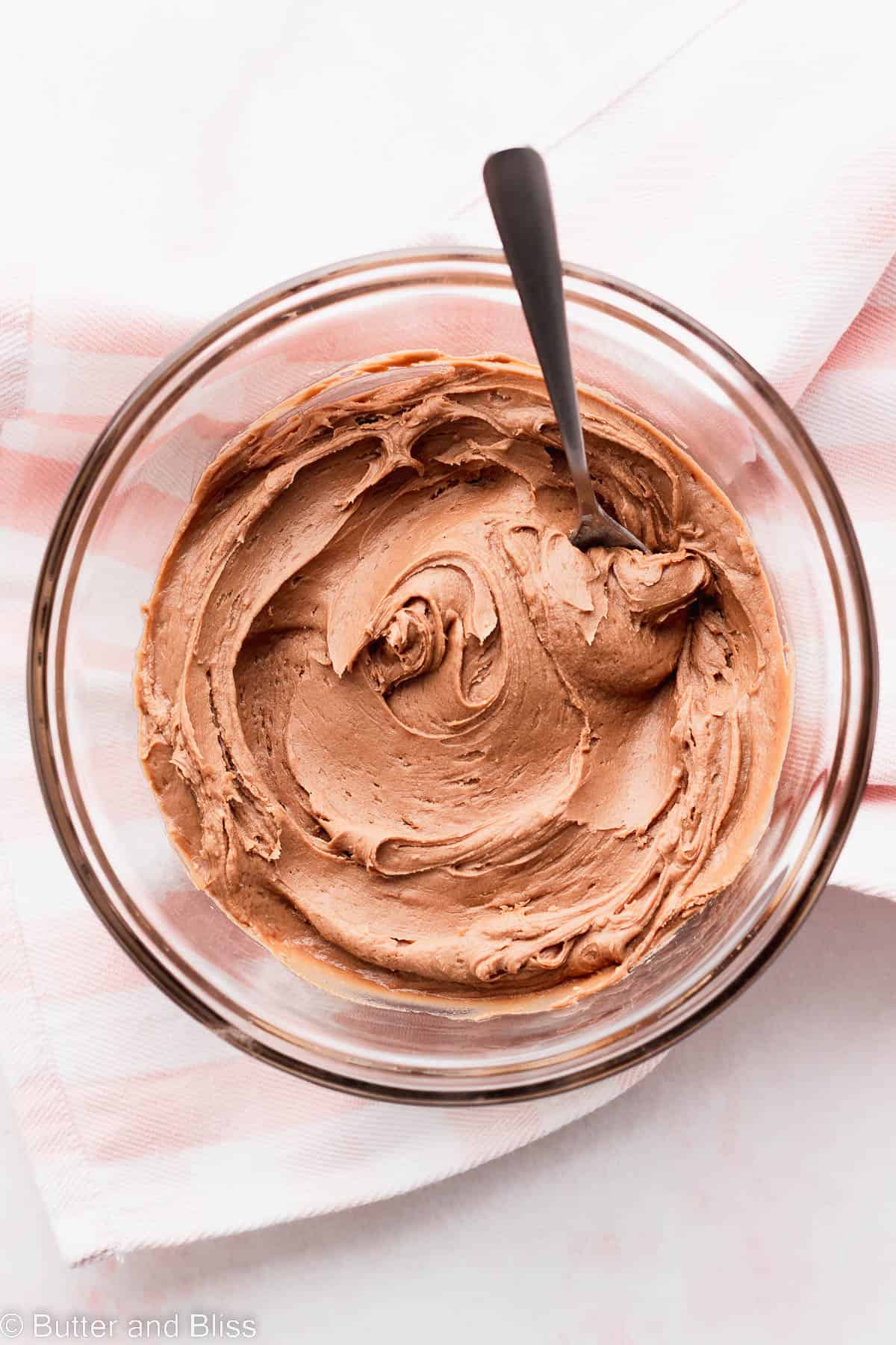 Ultra rich and creamy chocolate fudge frosting swirled in a small glass bowl on a table.