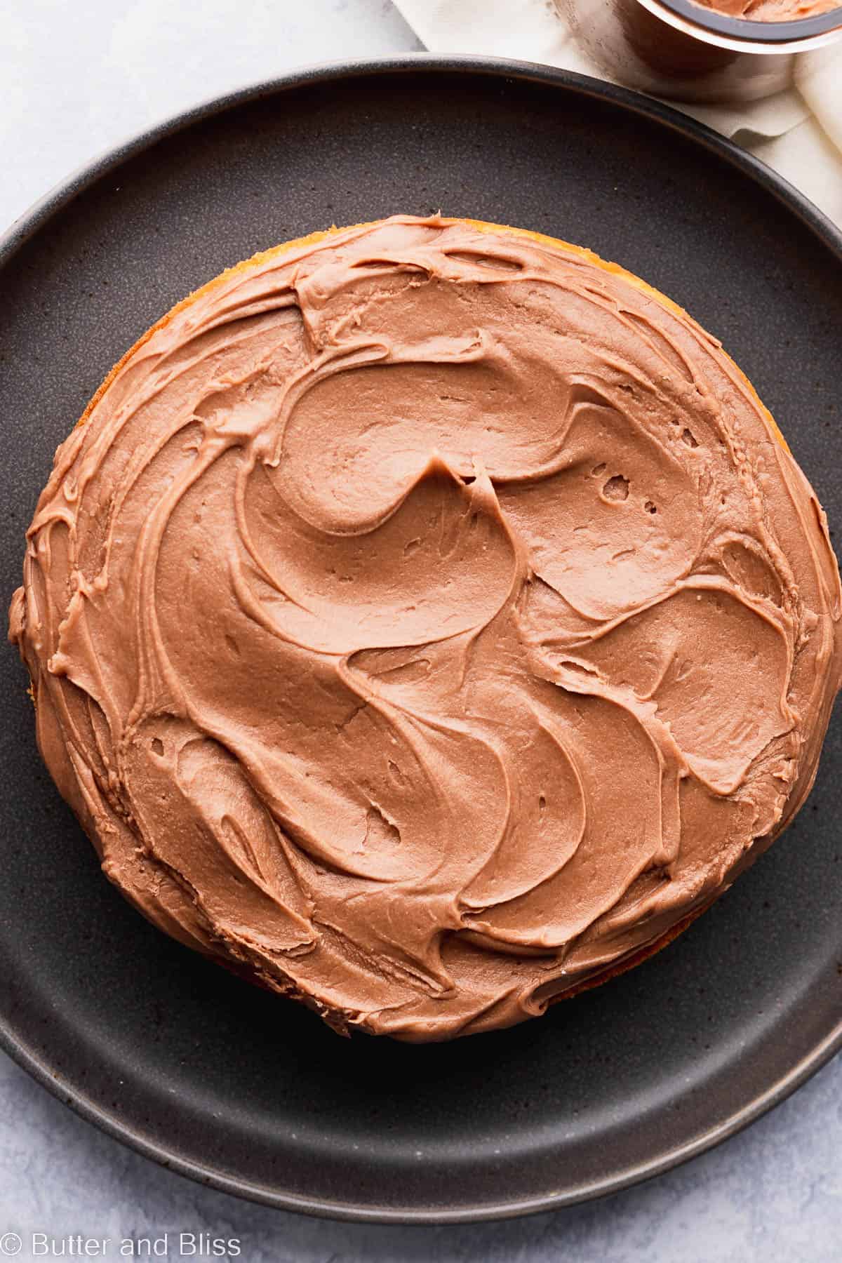 Chocolate fudge frosting on a mini vanilla cake set on a black plate.