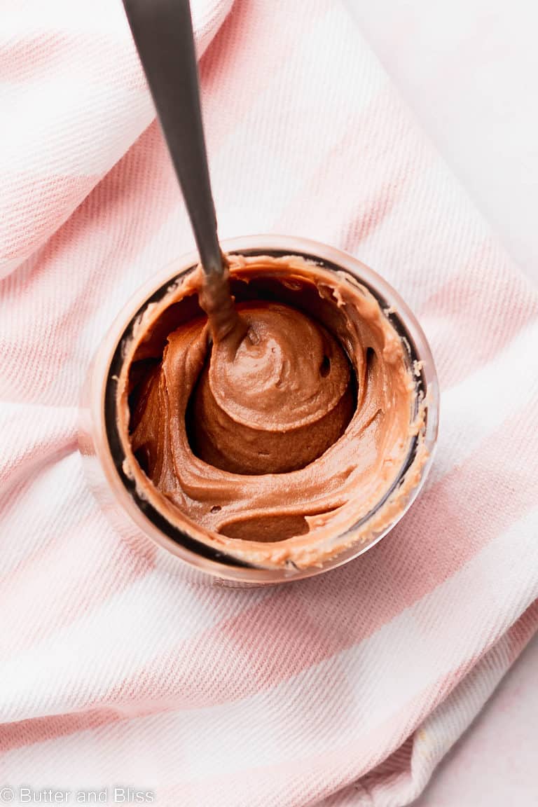 Creamy fudge frosting in a small jar with a spoon.