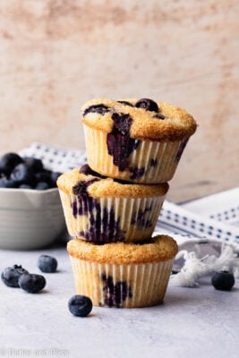Gluten free blueberry muffins stacked on top of each other next to a bowl of blueberries.