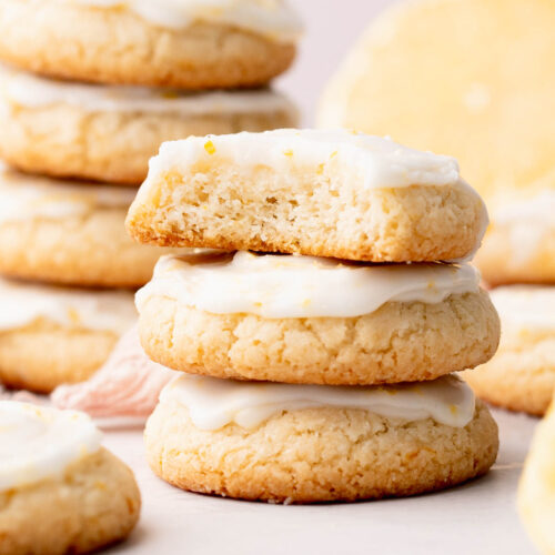 A short stack of glazed lemon drop shortbread cookies with a bite out of one.