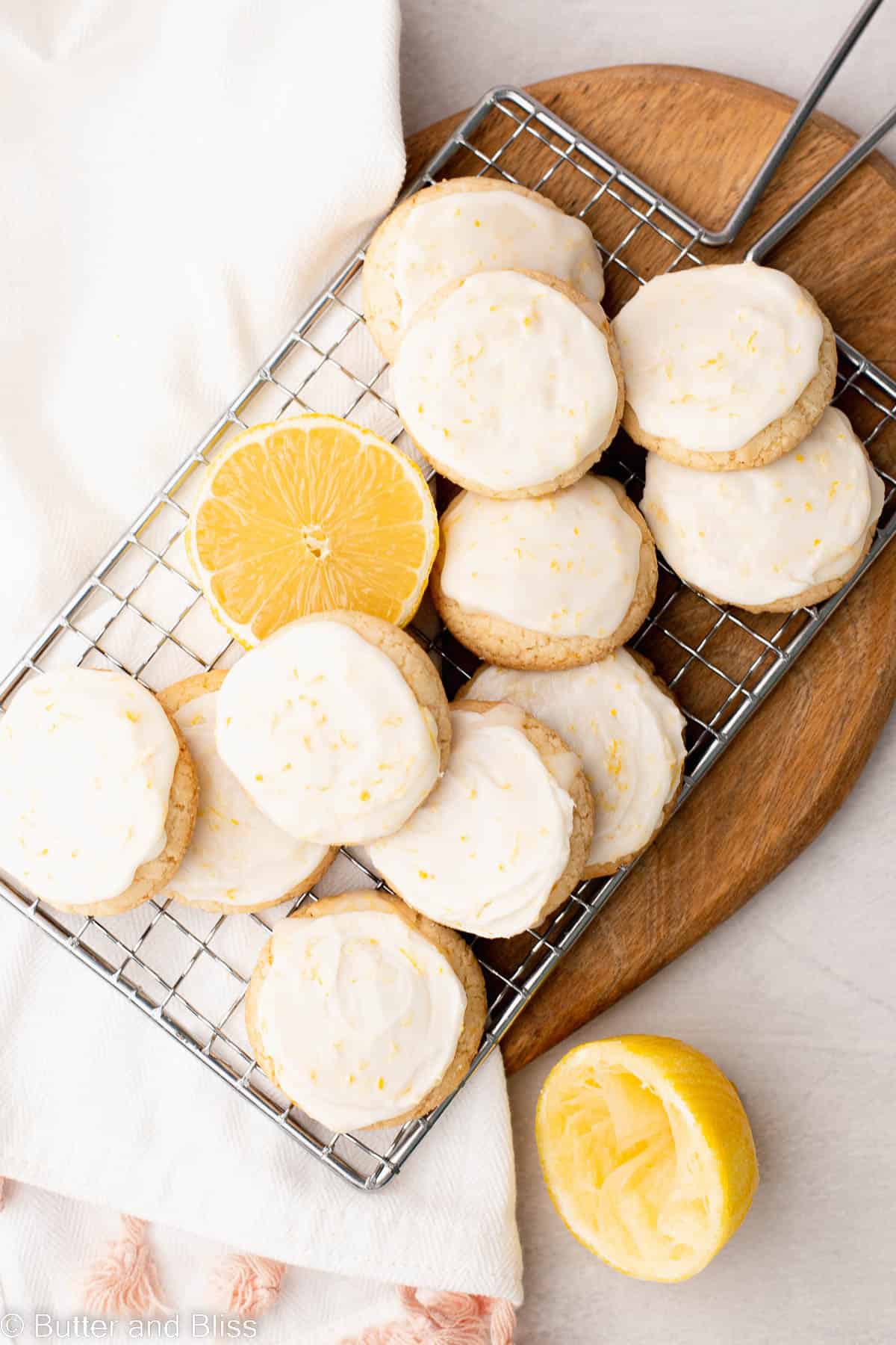 Glazed gluten free lemon drop cookies stacked in a pile on a wire cooling rack on a table.