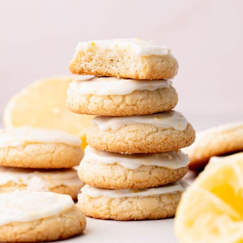 Lemon glazed lemon shortbread cookies arranged in stacks on a table with lemons.