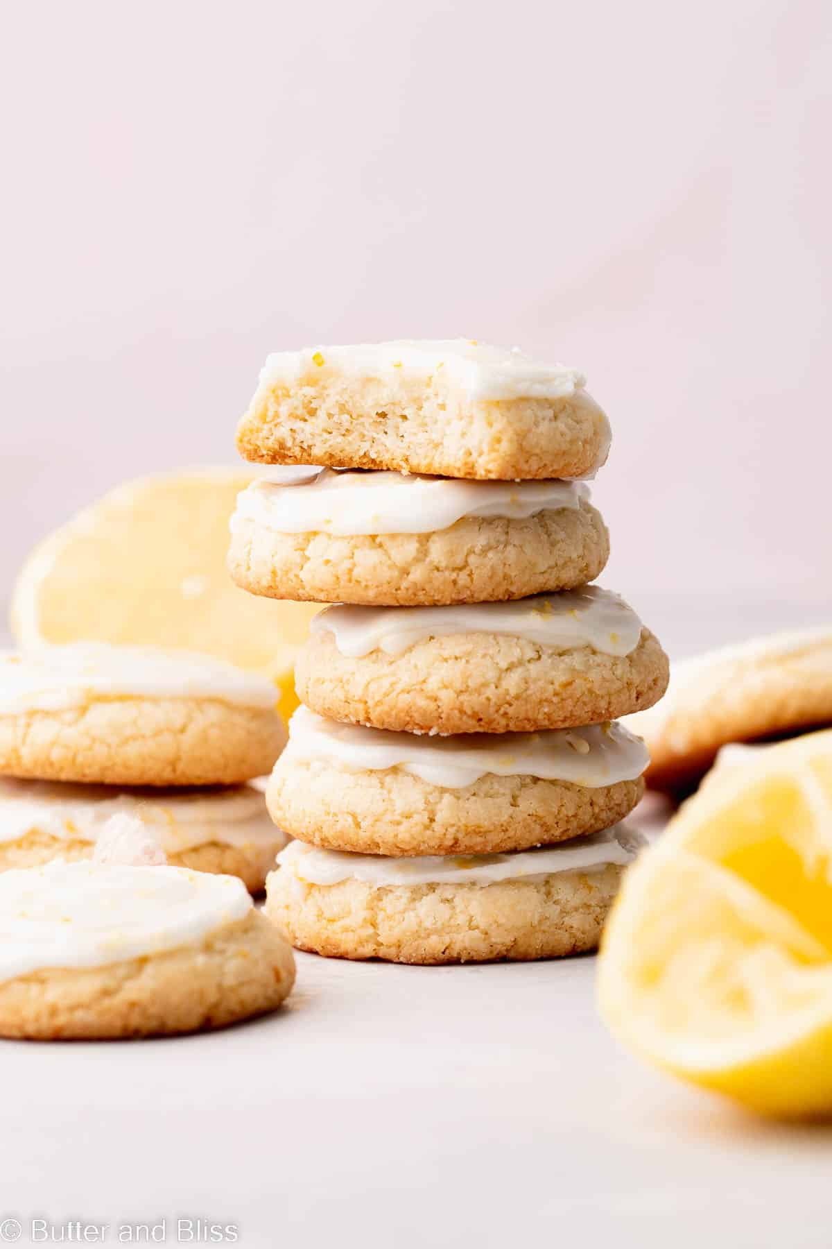 Lemon glazed lemon shortbread cookies arranged in stacks on a table with lemons.