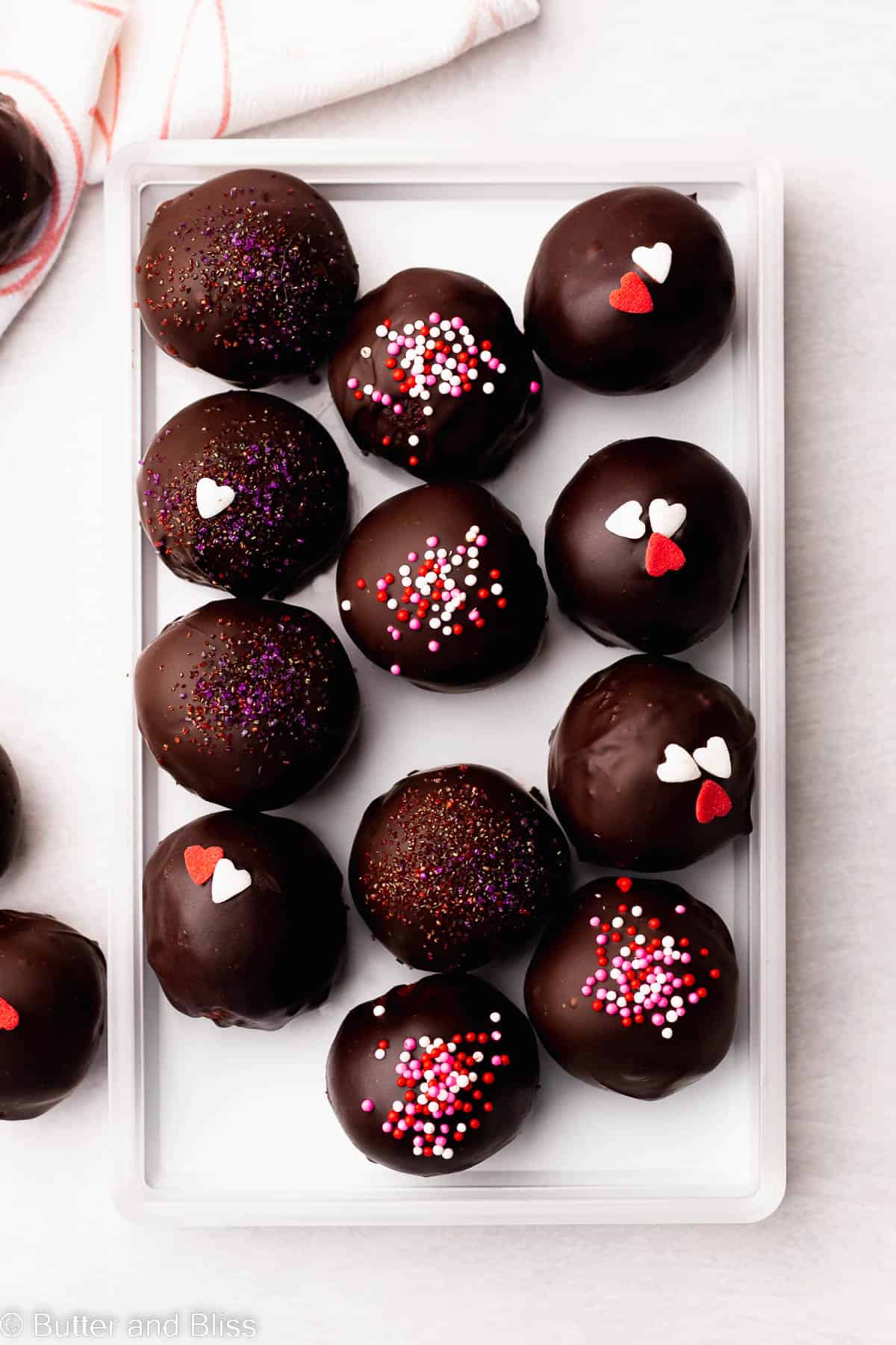 Gluten free cake truffles covered in chocolate and sprinkles arranged in a white tray.