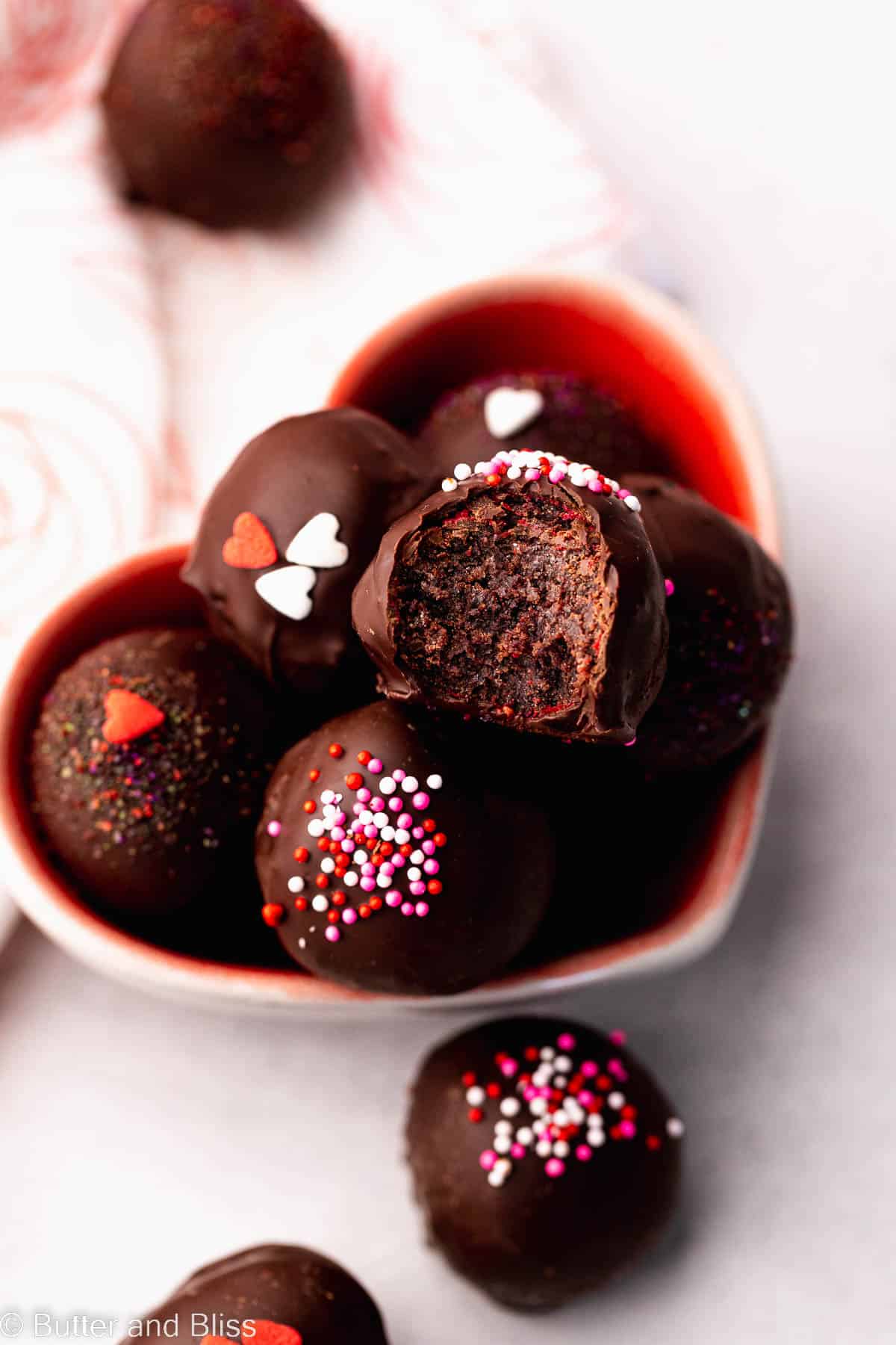 Cake truffles stacked in a heart shaped bowl with a bite out of the top one.