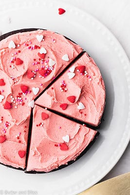 Small gluten free chocolate cake with strawberry frosting and sprinkles on a white plate.