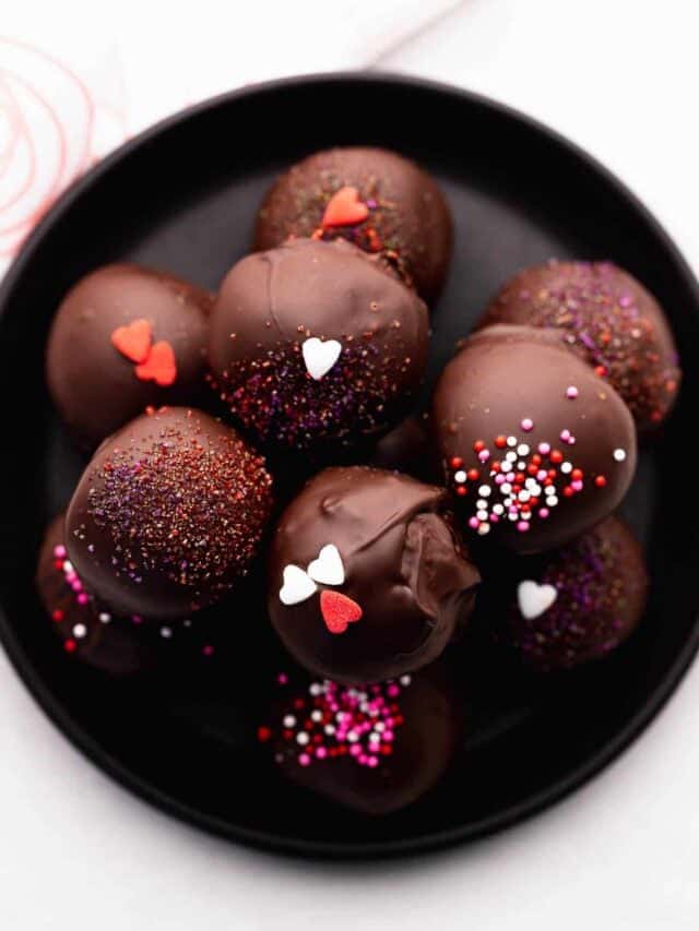 Cake truffles srpinkles neatly stacked on a black plate.