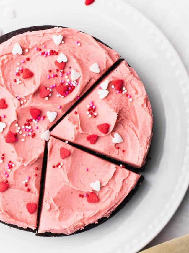 Small gluten free chocolate cake with strawberry frosting and sprinkles on a white plate.