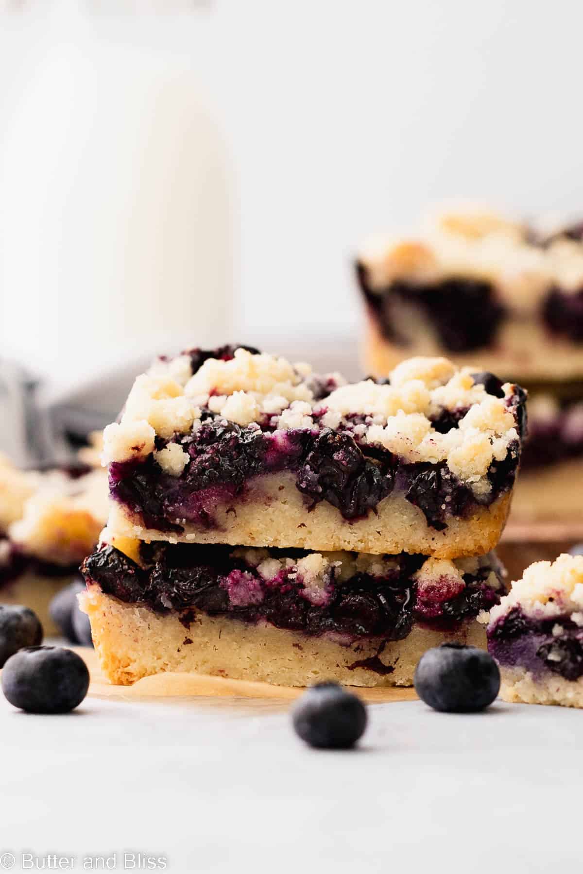 Two blueberry crumble bars with gooey blueberry filling stacked on a table.