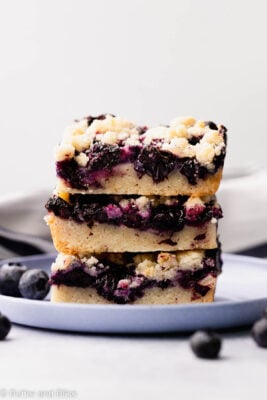 Three perfectly stacked gooey blueberry gluten free crumble bars on a blue plate.