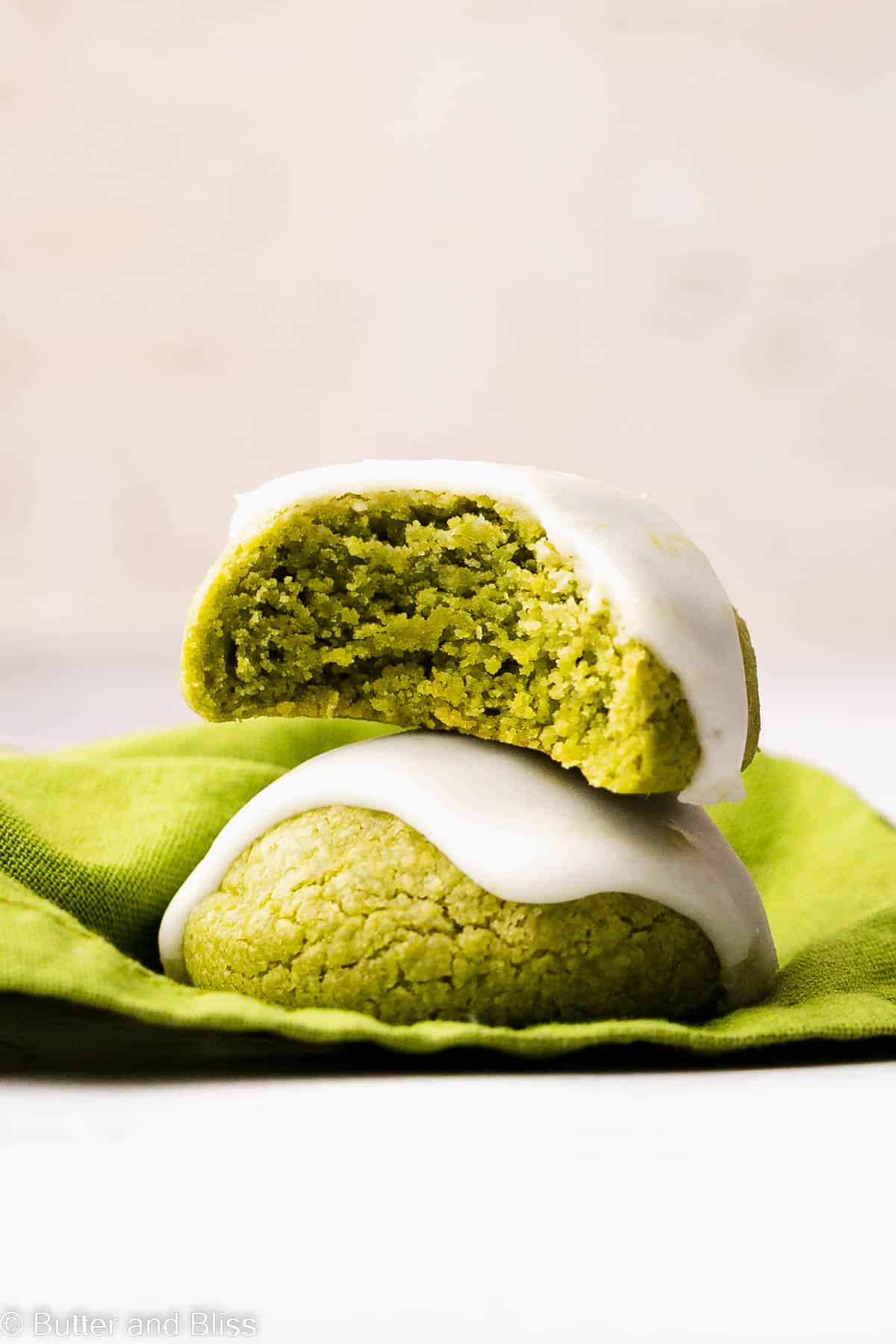 Bite shot of a beautiful lemon iced gluten free matcha cookie stacked on another on a table.