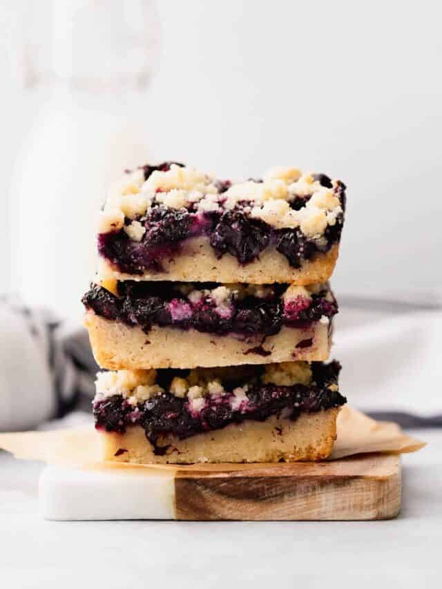 Gluten free blueberry crumble bars in a short stack on a small wooden plate on a table.
