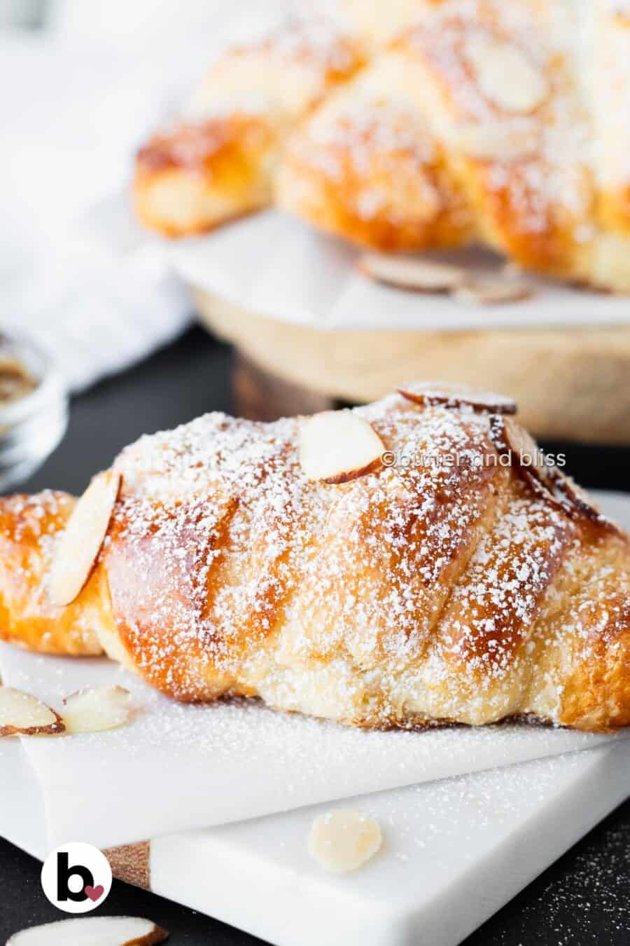 Single almond croissant with sliced almonds and powdered sugar on a small plate.