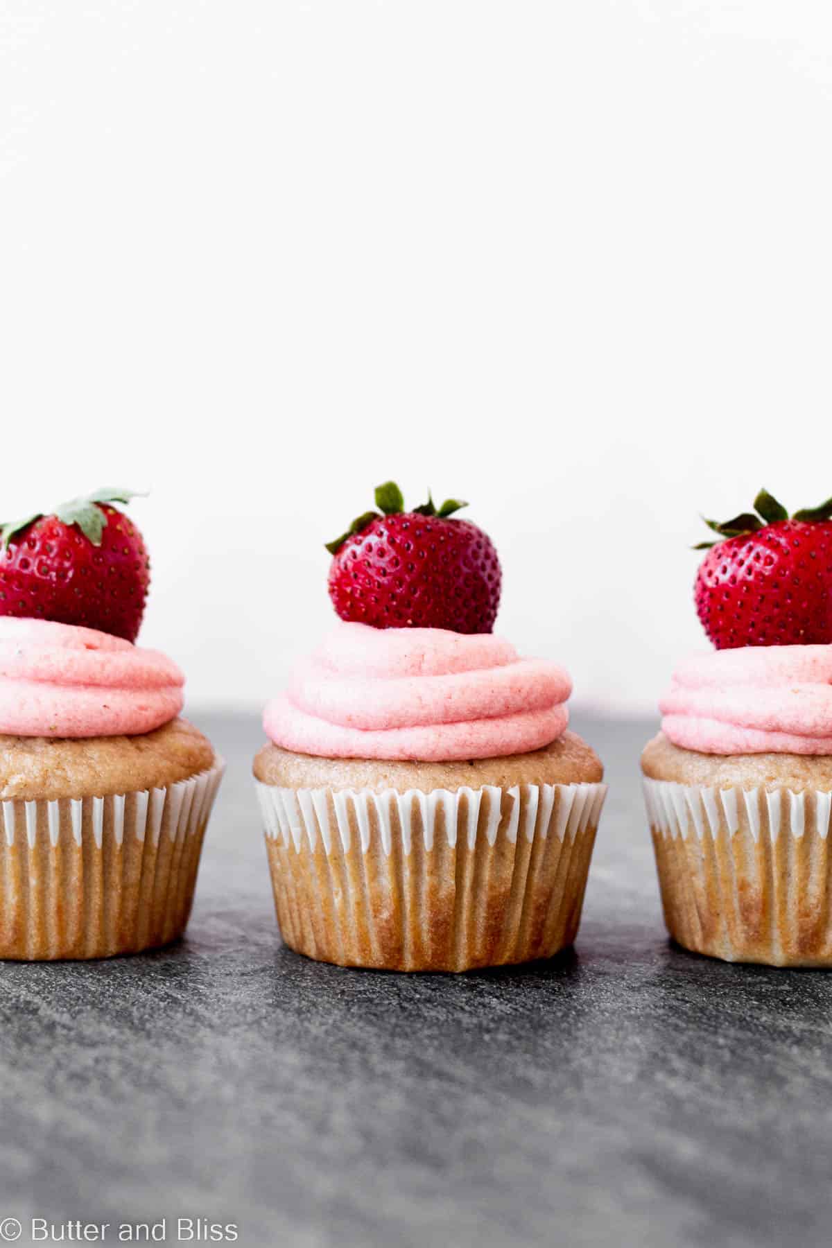 A row of three pretty little strawberry cupcakes with strawberry garnish.