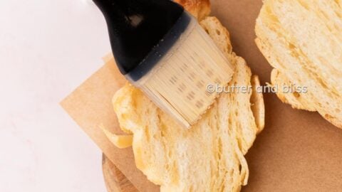 Hand brushing simple syrup on a croissant half.