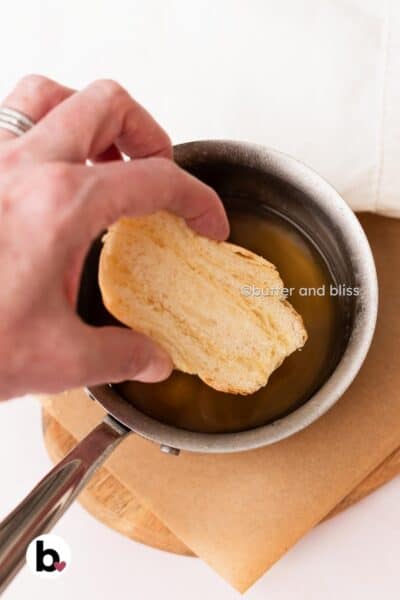 Hand dipping a croissant half into simple syrup.
