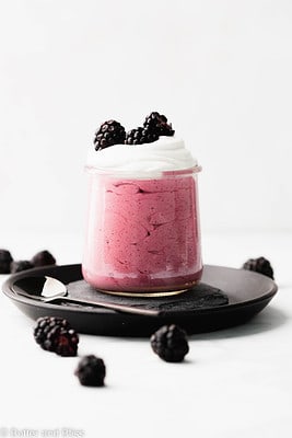 Incredibly pretty blackberry mousse in a serving glass set on a black plate.