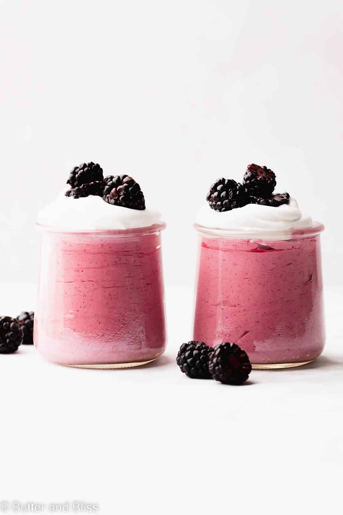 A pair of pretty serving glasses of blackberry mousse topped with whipped cream and fresh blackberries.