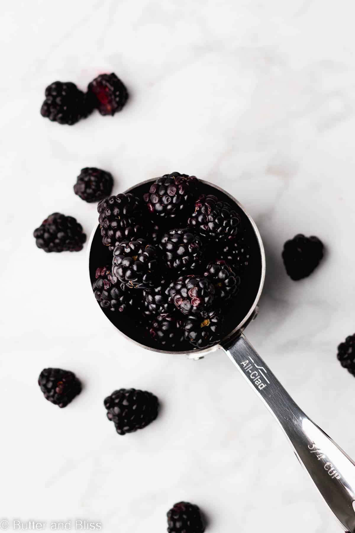 Fresh blackberries spilling out of a measuring cup.