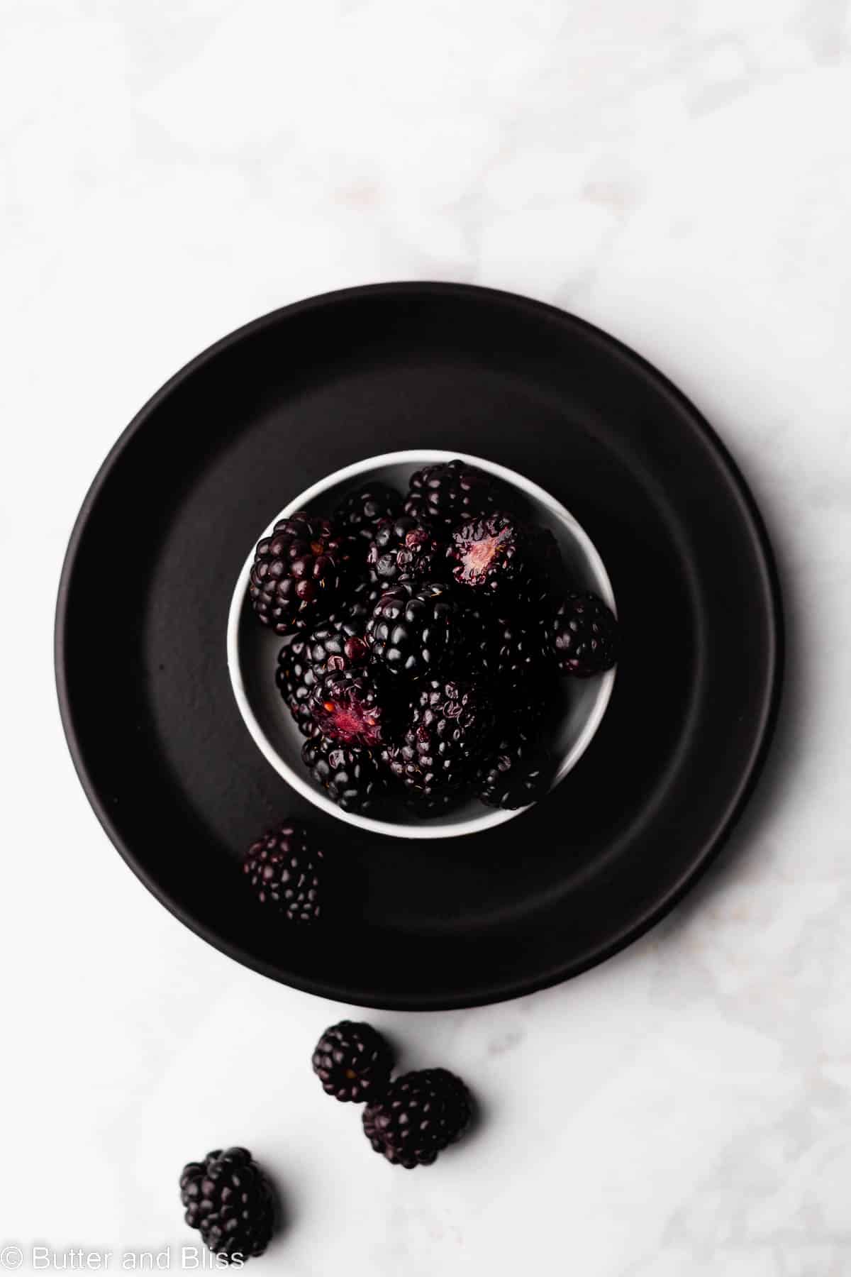 A dramatic photo of pretty blackberries in a bowl set on a black plate.
