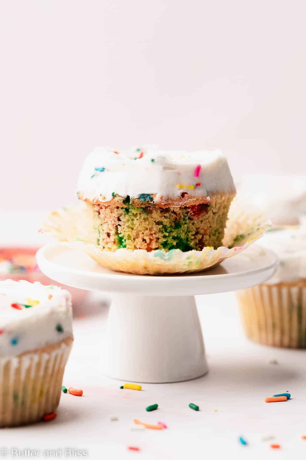 A fun little vanilla mini cake with the liner peeled back, set on a mini cupcake stand.