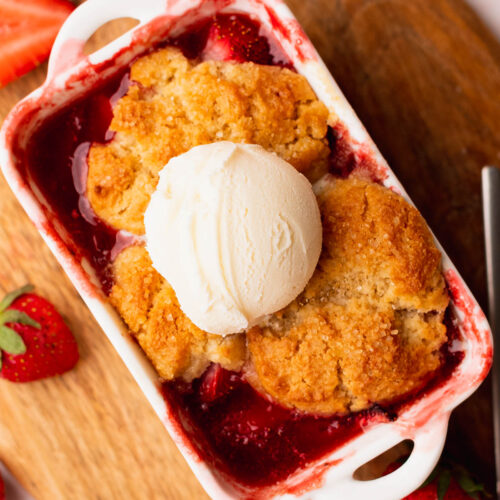 Close up of jammy strawberry cobbler in a pretty mini baking dish and topped with ice cream.