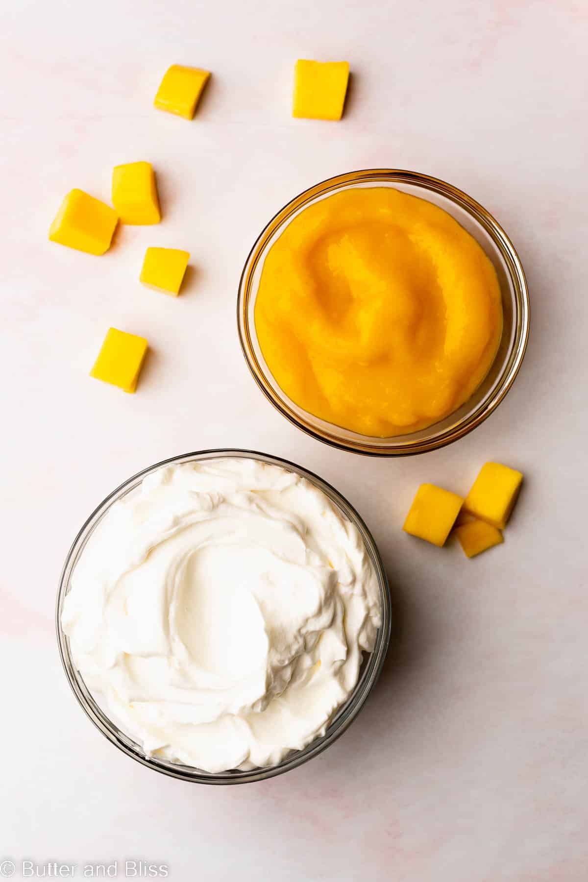 Velvety mango puree in a bowl next to a bowl of whipped cream.