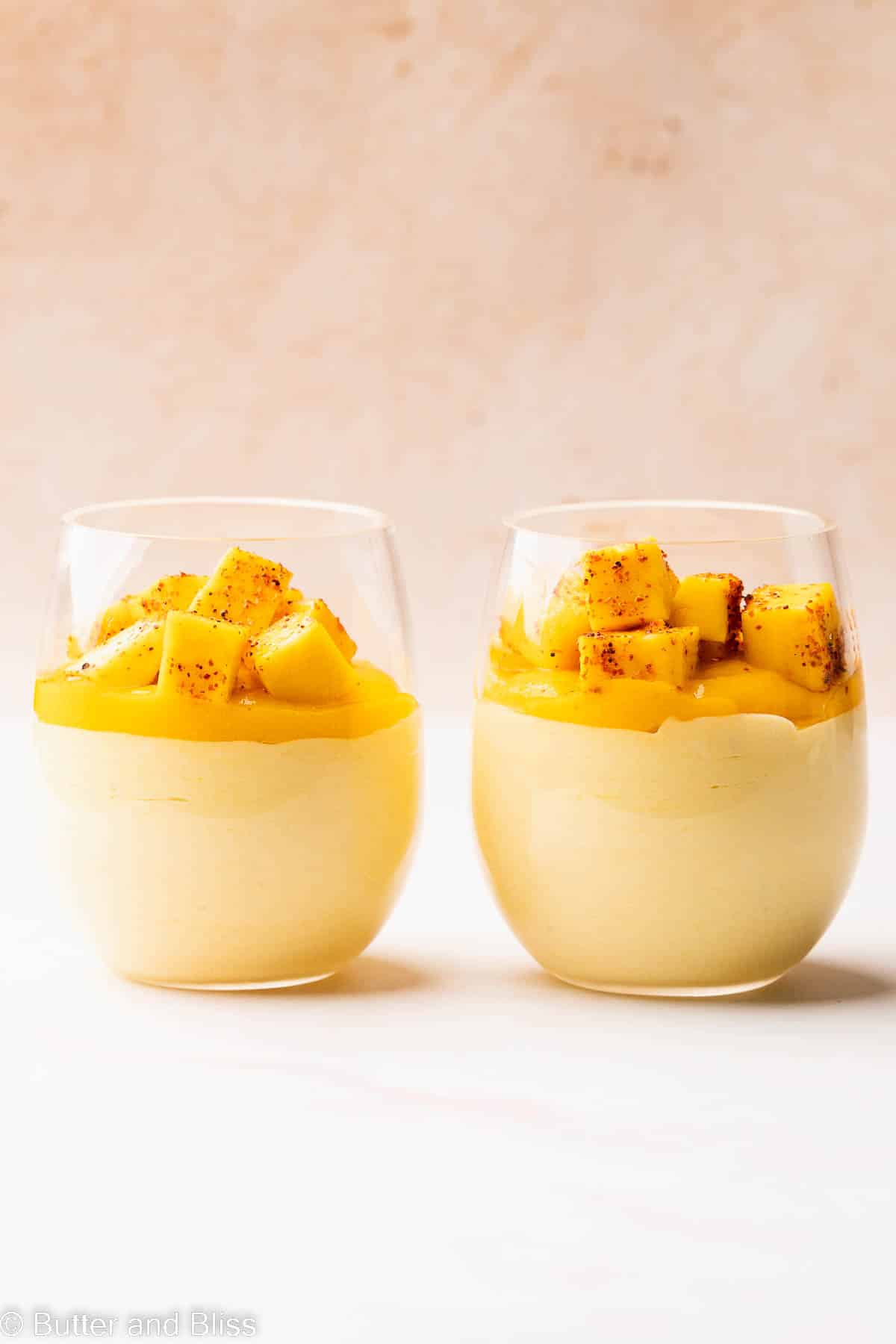 Parfait glasses full of mango mousse set side by side on a table.