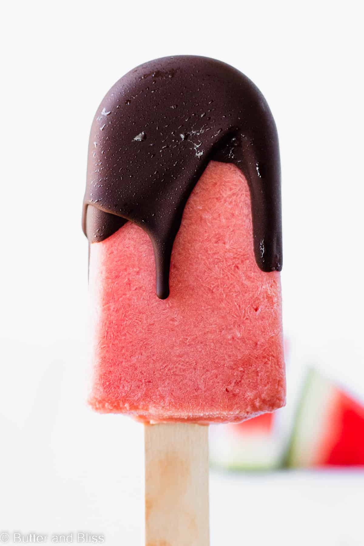 Single watermelon popsicle close up with drippy chocolate shell.