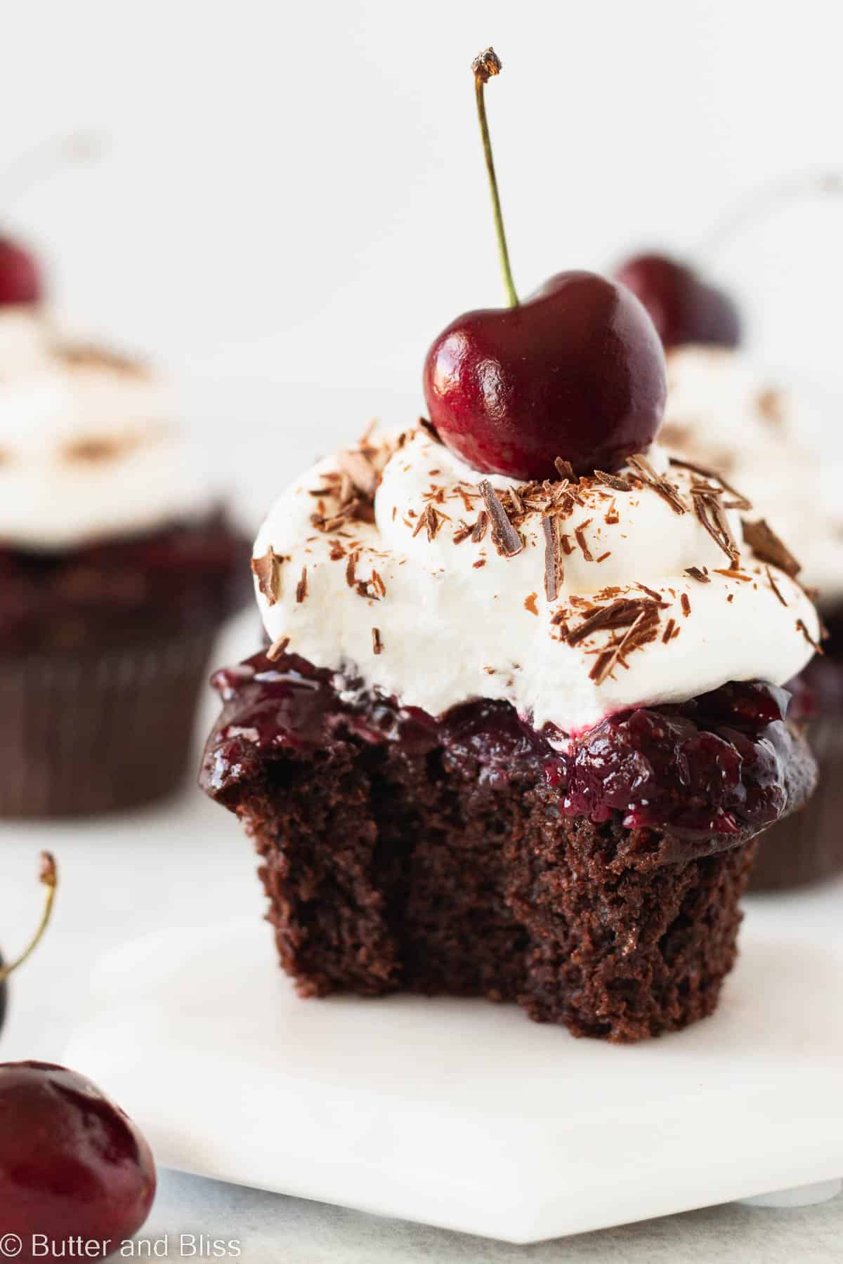 Single black forest cupcake with a bite on a small white plate.