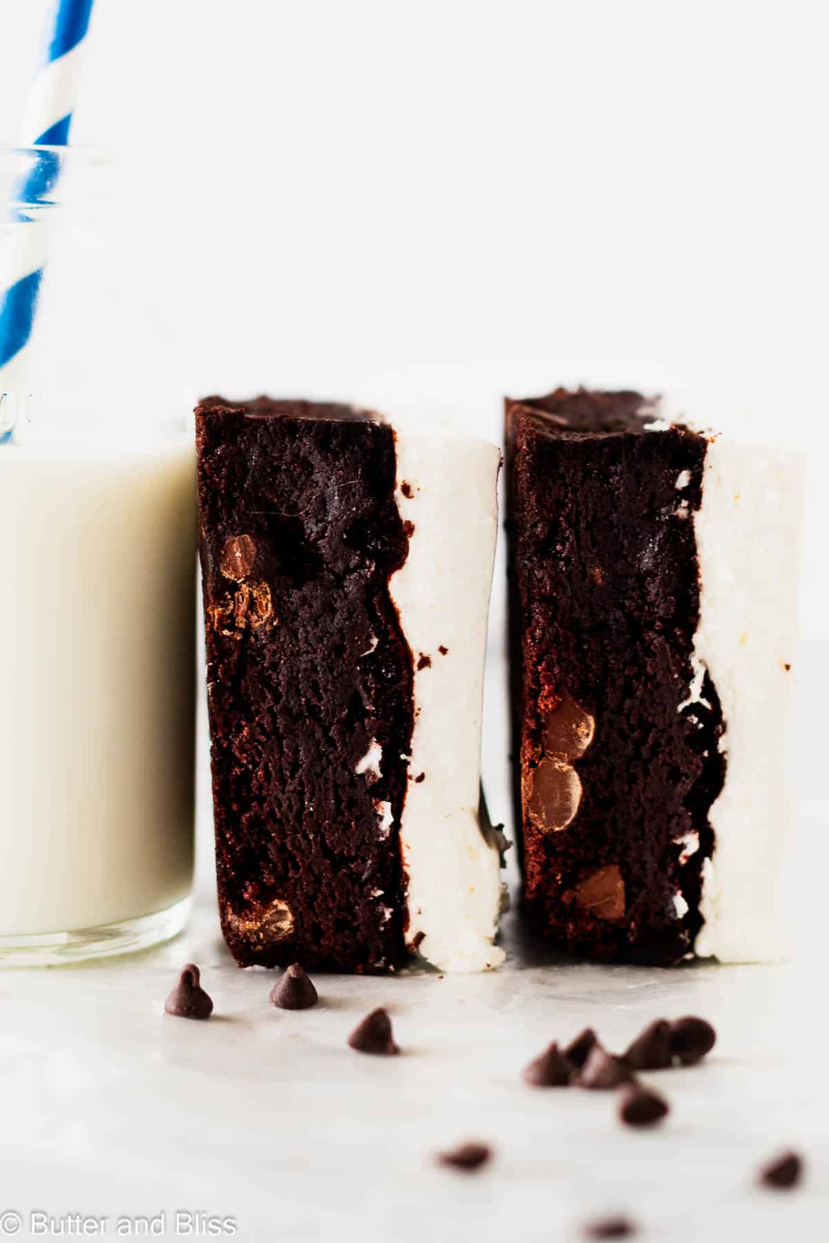 Two brownies with whipped topping propped against a glass of milk.