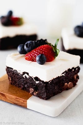 Single brownie with whipped topping and fruit garnish on a small wooden plate.
