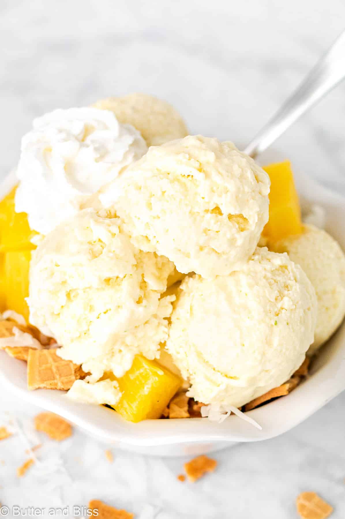 Pina colada ice cream sundae with fresh fruit and whipped cream in a white bowl.