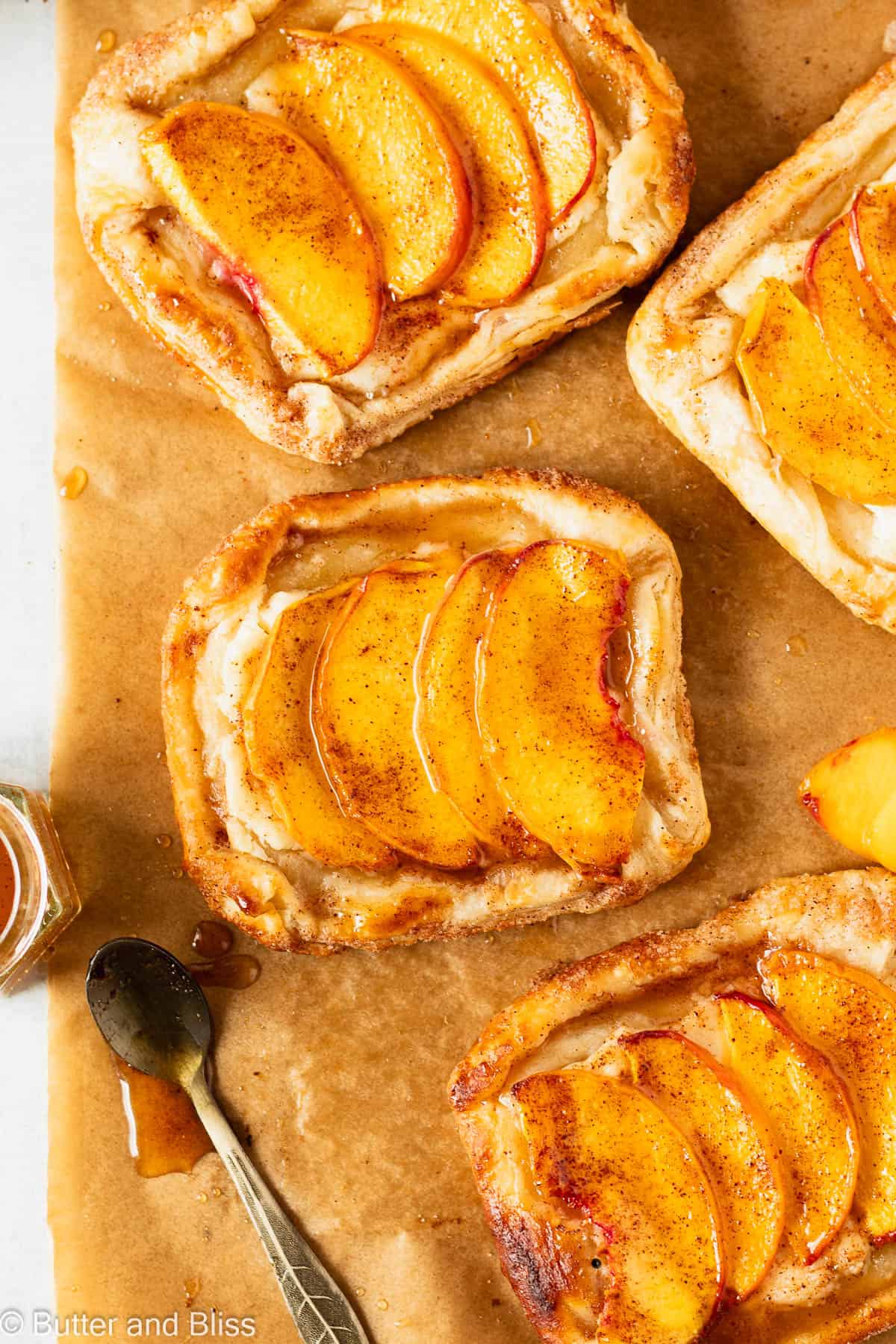 Freshly baked mini peach and cream cheese tarts on parchment paper with honey drizzle.