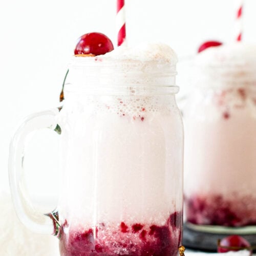 Black cherry coconut cream soda in a mug on a coaster surrounded by cherries.
