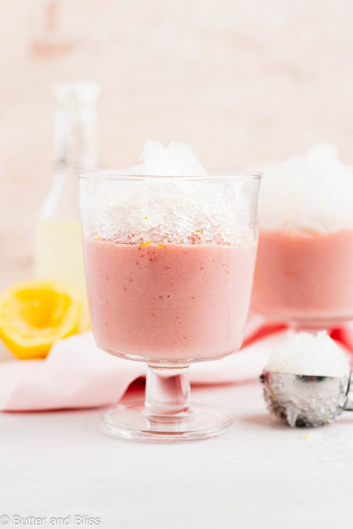 Layered lemonade granita and strawberry pudding in a parfait glass on a table.